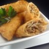 A close-up of crispy egg rolls by Owl Creek Farm, one cut open to reveal its savory filling, garnished with fresh parsley on a pristine white dish.