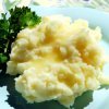 Mashed potatoes topped with butter, garnished with parsley, served on a blue plate by Owl Creek Farm.