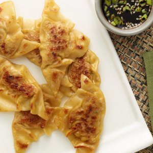 Pan-fried dumplings from Owl Creek Farm rest on a white plate, accompanied by a side of dipping sauce.