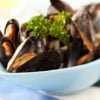 A bowl of mussels by Owl Creek Farm, garnished with parsley in a blue dish, resting on a blue and white napkin.