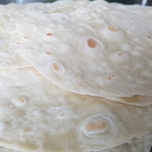 Close-up of a stack of homemade flour tortillas by Owl Creek Farm on a reflective surface.