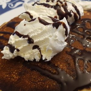 Pancake with whipped cream and chocolate syrup on a decorative plate, crafted by Owl Creek Farm.