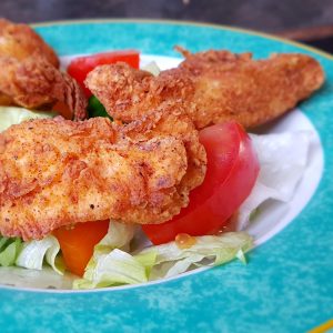a photo of breaded and pan fried chicken strips on top of lettuce and tomatoes