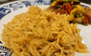a photo of a plate with seasoned rice in the foreground and vegetables in the background by owlcreek.ca